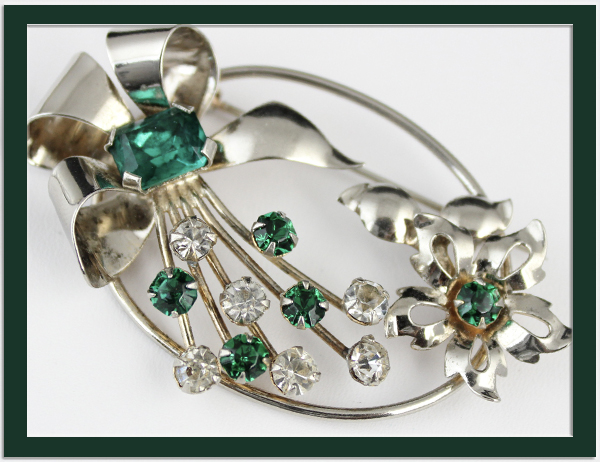 A LOVELY STERLING BROOCH in a floral design with emerald green and clear rhinestones